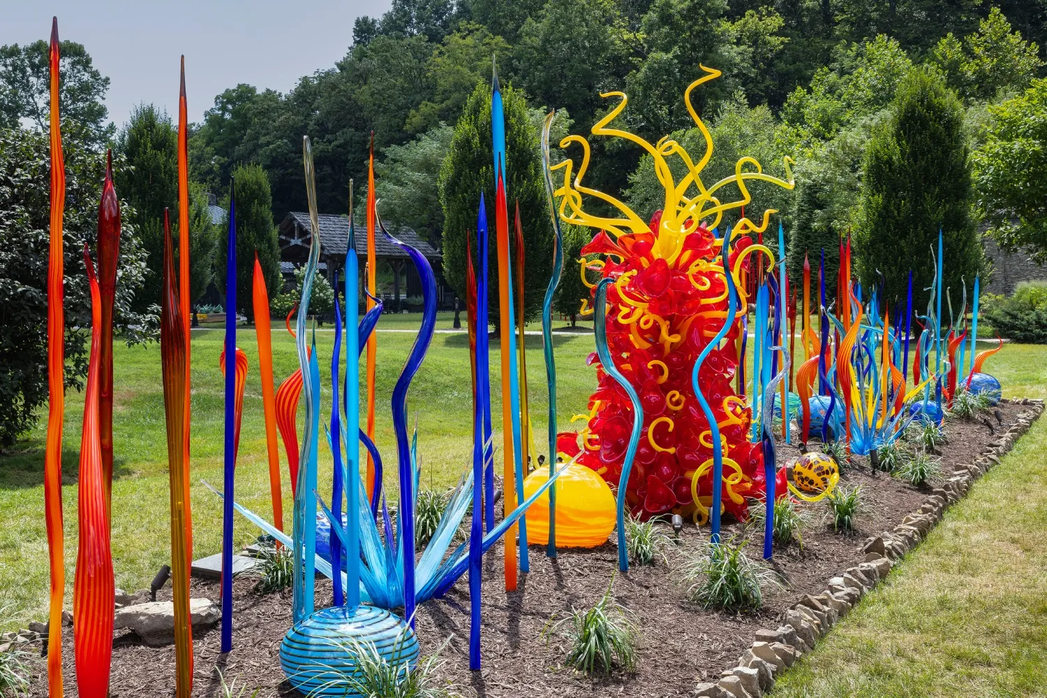 Vibrant glass sculptures of various colors and shapes arranged in a beautiful garden, creating a lively, artistic landscape.