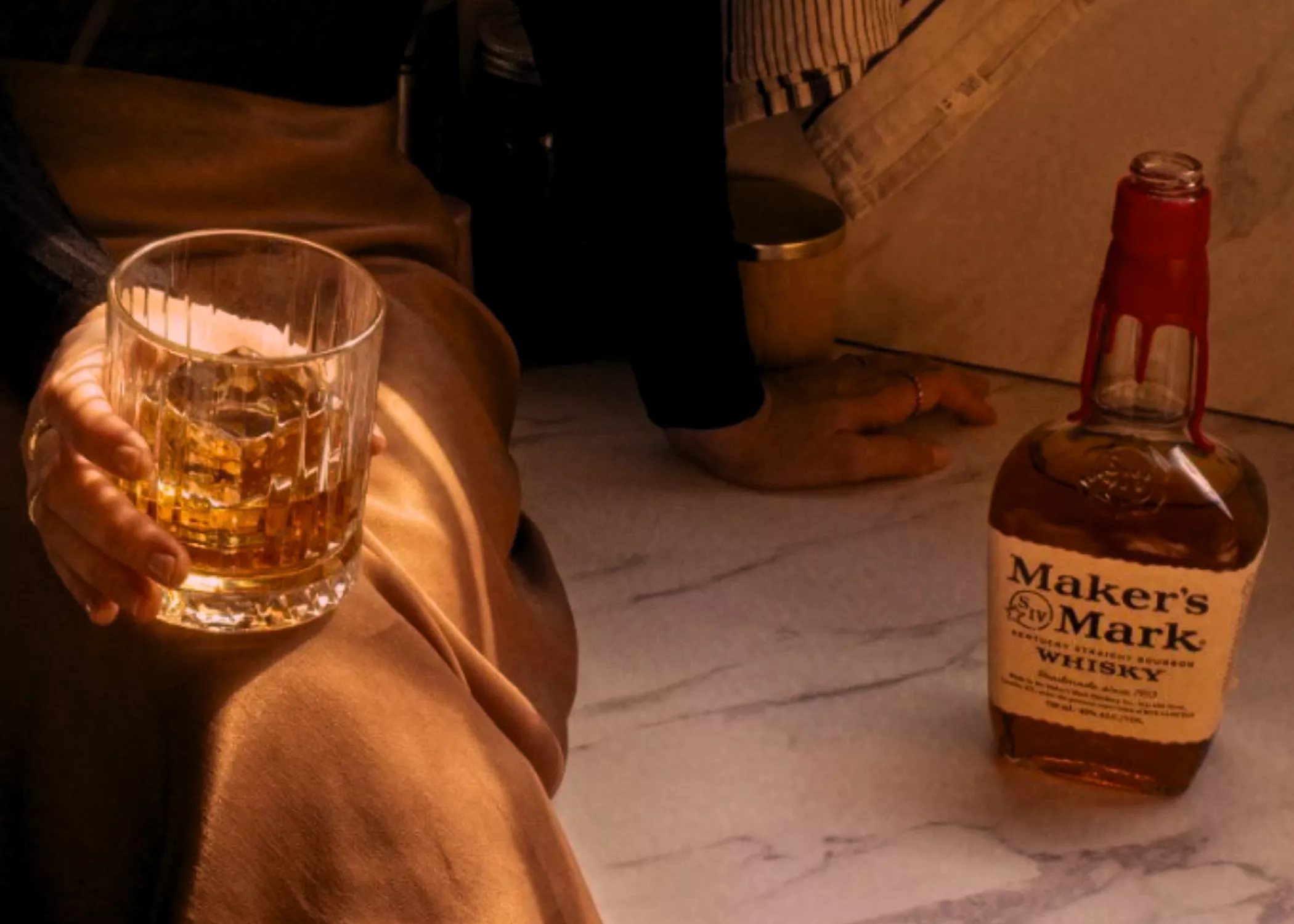 Man holding cocktail and sitting next makers mark classic bottle 